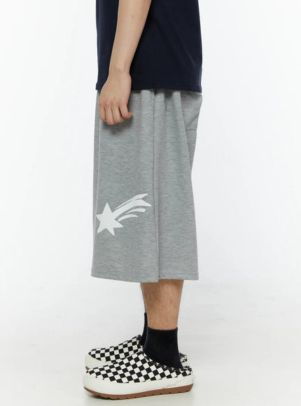 Men's Shooting Star Printed Shorts (Gray) IL509 Gray side view on model highlighting oversized wide-leg silhouette, side seam pocket, and white shooting star print on lower leg panel