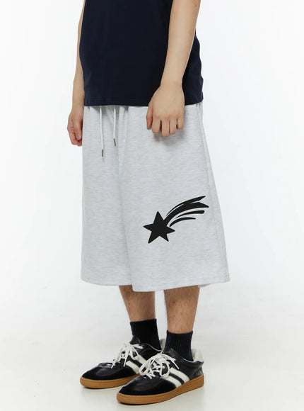 LEWKIN Men's Shooting Star Printed Shorts (Light Gray) IL509 Light gray side view on model, wide-leg silhouette with shooting star print, drawstring waist, paired with navy tee