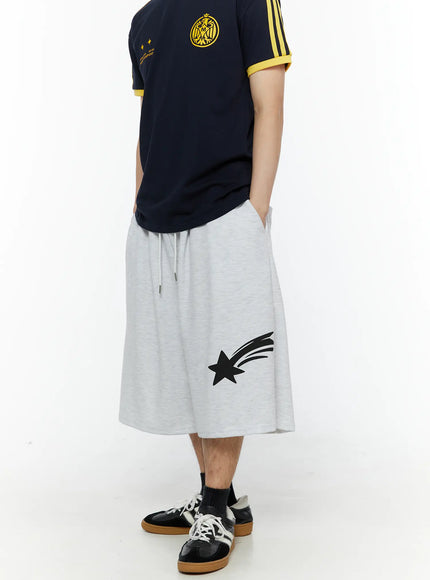 Men's Shooting Star Printed Shorts (Light Gray) IL509 Light gray side view on model styled with navy soccer jersey, shooting star print visible, hand in pocket