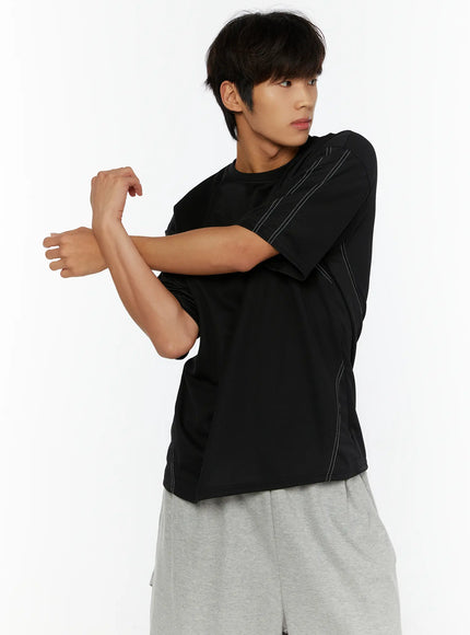 Men's Stitched T-Shirt IL513 Black side-angle shot on male model with arms crossed showing white contrast stitching on sleeve seam