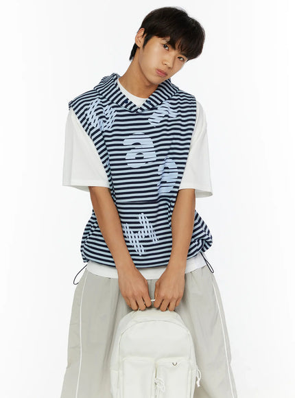 Men's Striped Graphic Hoodie IL510 Light blue front seated shot on male model leaning on white backpack, showing layered hem and drawstring at waist with graphic print