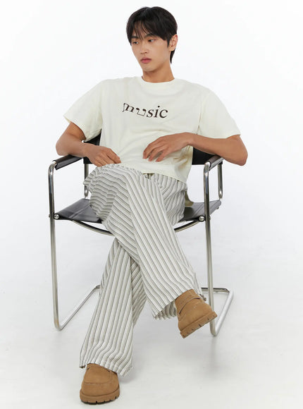 Men's Striped Wide-Leg Pants IL515 Light beige lifestyle shot on male model seated on chrome chair with legs crossed, hands resting on lap, looking to side