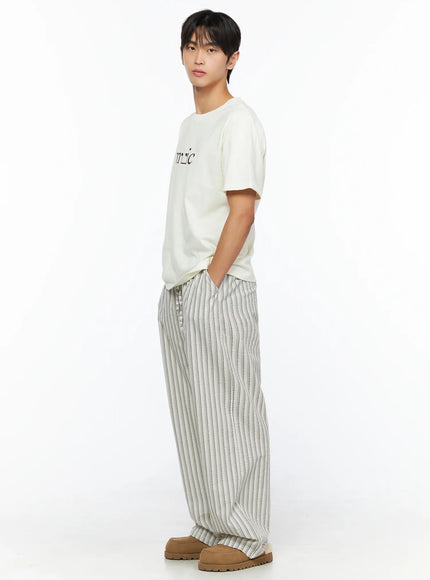 Men's Striped Wide-Leg Pants IL515 Light beige side shot on male model in three-quarter view standing, hands in pockets, styled with cream graphic tee and tan slippers