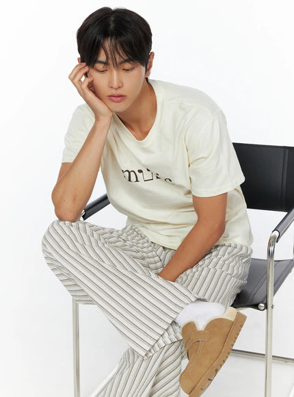 Men's Striped Wide-Leg Pants IL515 Light beige editorial shot on male model seated on chrome chair, head resting on hand in relaxed pose, showing stripe texture