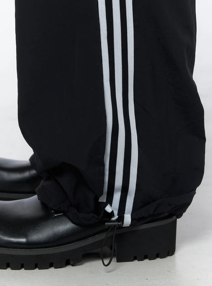 Men's Striped Wide Leg Track Pants IL502 Black close-up detail of hem showing adjustable drawcord ankle cinch and white triple stripe on lightweight nylon fabric