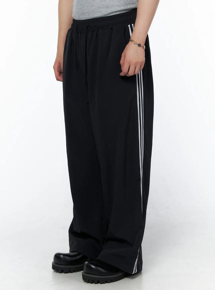 LEWKIN Men's Striped Wide Leg Track Pants IL502 Black side shot on model showing white triple side stripes elastic drawstring waist and wide leg silhouette
