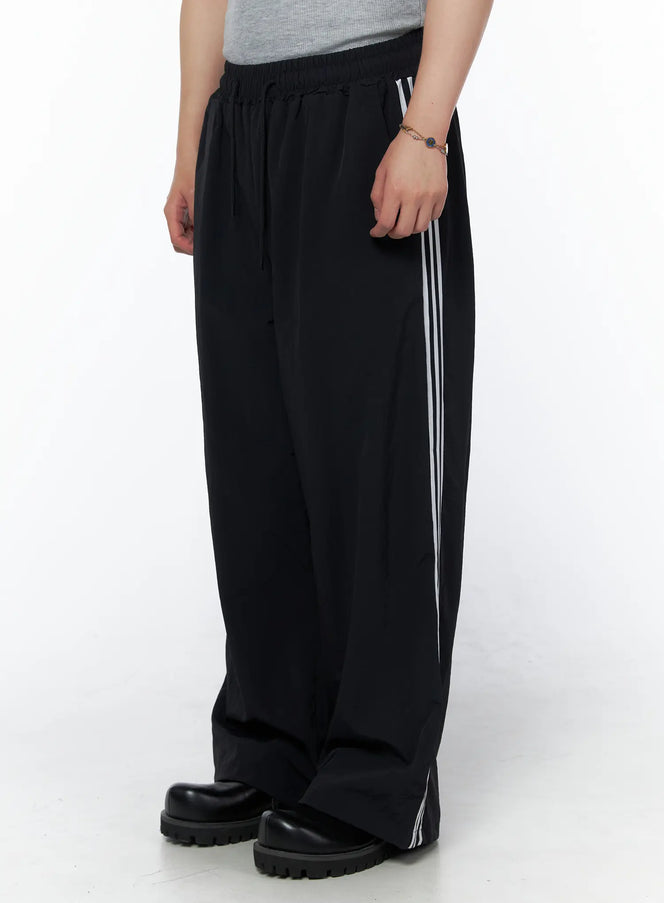 LEWKIN Men's Striped Wide Leg Track Pants IL502 Black side shot on model showing white triple side stripes elastic drawstring waist and wide leg silhouette