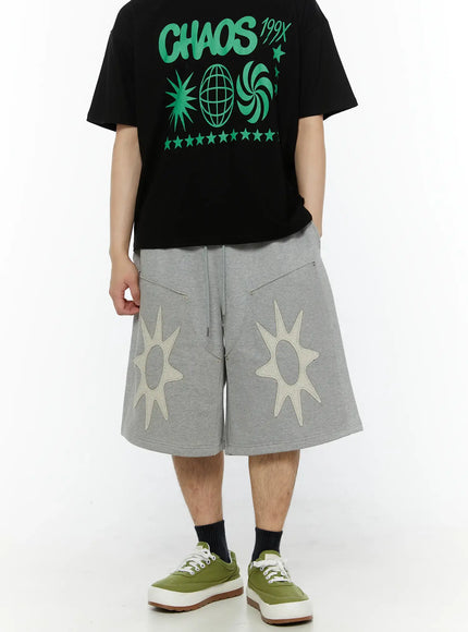 Men's Sun Embroidered Shorts (Gray) IL509 Gray back-angle view on model wearing black graphic tee, wide-leg silhouette with cream sun patch appliqués visible