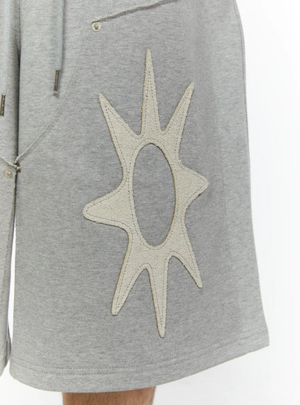 Men's Sun Embroidered Shorts (Gray) IL509 Gray close-up detail of cream sun burst appliqué patch with open oval center and embroidered border on heathered gray cotton