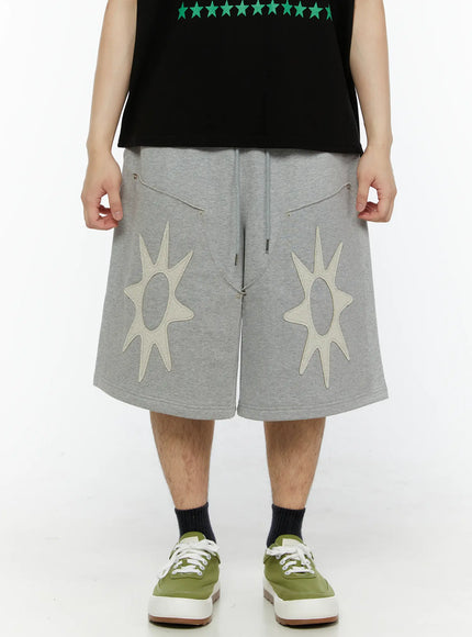 LEWKIN Men's Sun Embroidered Shorts (Gray) IL509 Gray front view on model size M/L with cream star appliqués and drawstring waist, styled with black tee and green sneakers