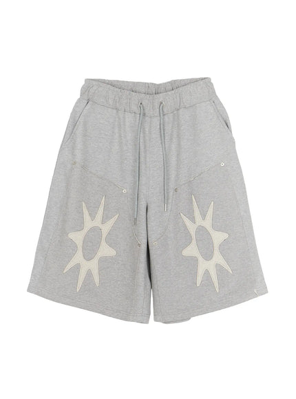 Men's Sun Embroidered Shorts (Gray) IL509 Gray flat-lay front view showing elastic drawstring waistband, twin cream sun appliqués, rivet details, and relaxed wide-leg silhouette