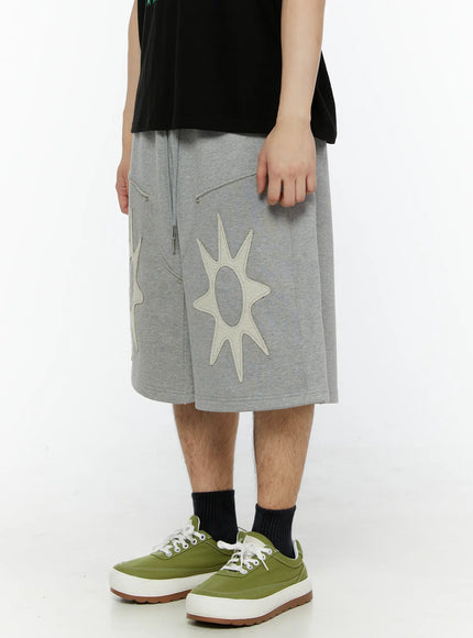 Men's Sun Embroidered Shorts (Gray) IL509 Gray side view on model showing relaxed wide-leg fit, drawstring waist, and single cream sun appliqué with textured stitching detail