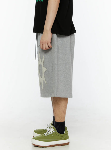 Men's Sun Embroidered Shorts (Gray) IL509 Gray side view on model showing right leg silhouette, partial cream sun appliqué, drawstring ties, and green sneakers