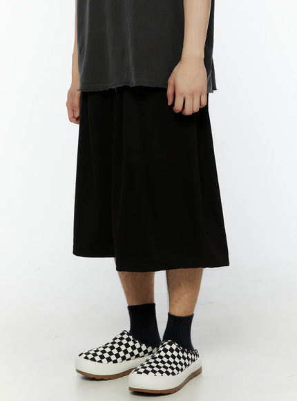 Men's Swirl Print Back Pocket Shorts (Black) IL509 Black side close-up shot on model showing wide flared leg drape and smooth cotton fabric texture with checkered slip-on shoes