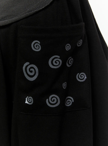 Men's Swirl Print Back Pocket Shorts (Black) IL509 Black full-body front shot on model raising arm styled with vintage graphic sleeveless tee headphones and checkered slip-on shoes