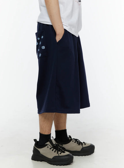 Men's Swirl Print Back Pocket Shorts (Dark Blue) IL509 Dark Blue side view on male model hand in pocket showing swirl print detail and wide-leg drop crotch cut