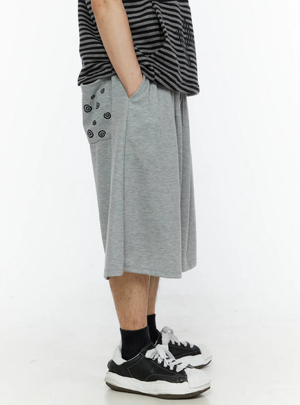 Men's Swirl Print Back Pocket Shorts (Gray) IL509 Gray side view on model highlighting black swirl pocket print hand in pocket showing voluminous wide-leg drop-crotch cut