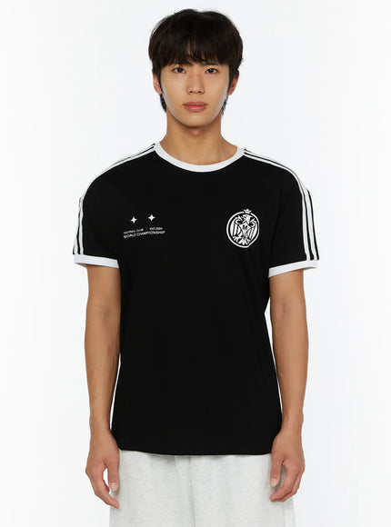 Men's Track Graphic T-Shirt IL507 Black front view on model, white three-stripe shoulders, white rib collar and cuffs, white eagle crest and World Championship print, grey pants