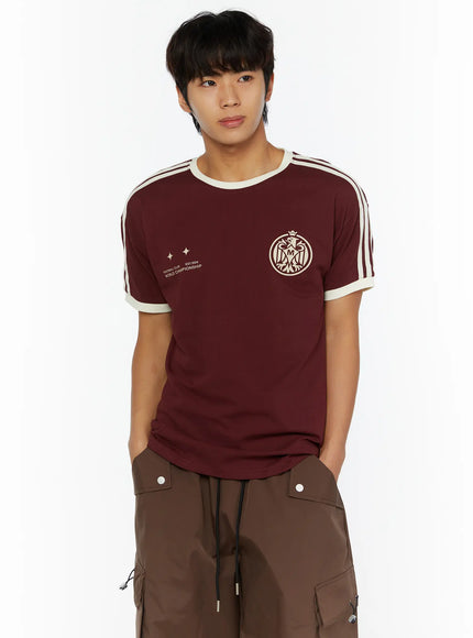Men's Track Graphic T-Shirt IL507 Burgundy cropped front on model hands in pockets, showing Football Club World Championship print and eagle crest graphic