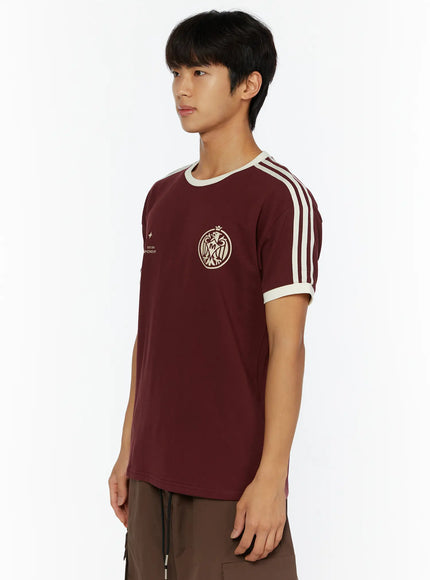 Men's Track Graphic T-Shirt IL507 Burgundy side view on model looking right, showing cream shoulder stripes, crest graphic and slim fit silhouette