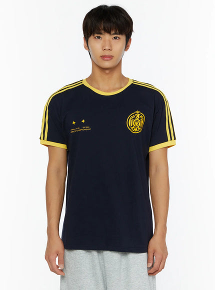 Men's Track Graphic T-Shirt IL507 Navy front view on model, yellow three-stripe shoulders, yellow rib collar and cuffs, eagle crest and World Championship print, grey pants