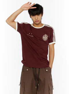 LEWKIN Men's Track Graphic T-Shirt IL507 Burgundy close-up front on model, hand raised to forehead, cream stripe sleeves, crest and World Championship print