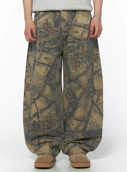 LEWKIN Men's Tree Graphic Wide Leg Pants IL502 Beige front close-up on model showing wide-leg silhouette and allover tree branch leaf camo print