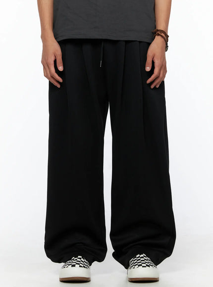 LEWKIN Men's Triple Tuck Sweatpants IL520 Black S/M front view on model wearing gray graphic tee and checkered sneakers, wide-leg silhouette with drawstring waist