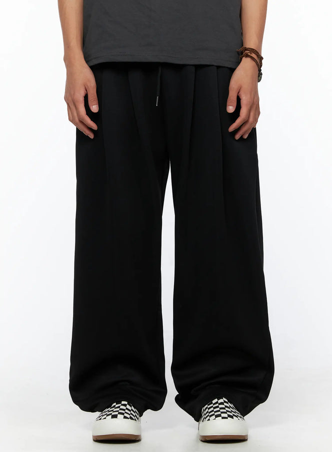 LEWKIN Men's Triple Tuck Sweatpants IL520 Black S/M front view on model wearing gray graphic tee and checkered sneakers, wide-leg silhouette with drawstring waist
