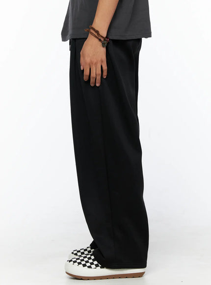 Men's Triple Tuck Sweatpants IL520 Black side view on model showing straight wide-leg profile, smooth fabric drape, and ankle-length hem with checkered sneakers