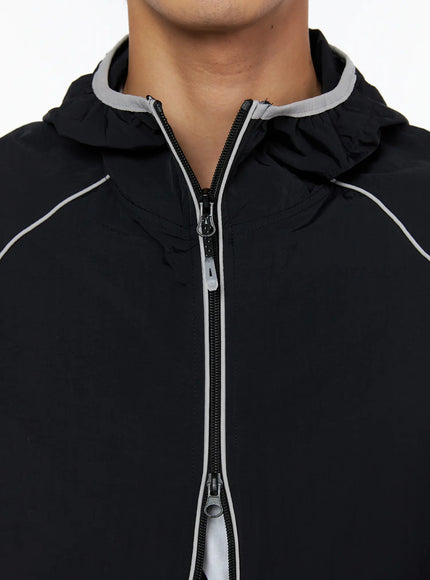 Men's Two-Tone Windbreaker IL528 Black close-up detail of dual zipper pull and grey contrast piping at neckline and hood attachment on model