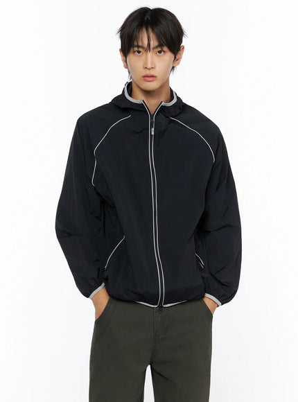 Men's Two-Tone Windbreaker IL528 Black front view on male model, hands in pockets, hooded zip-up nylon jacket with white reflective piping