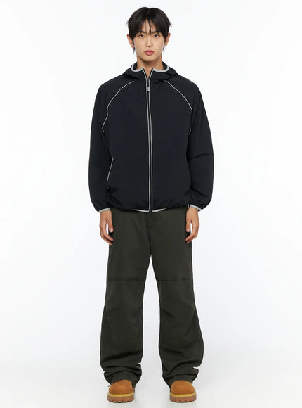 Men's Two-Tone Windbreaker IL528 Black full-body front on male model standing straight, hooded windbreaker with grey trim hem and cuffs, olive pants