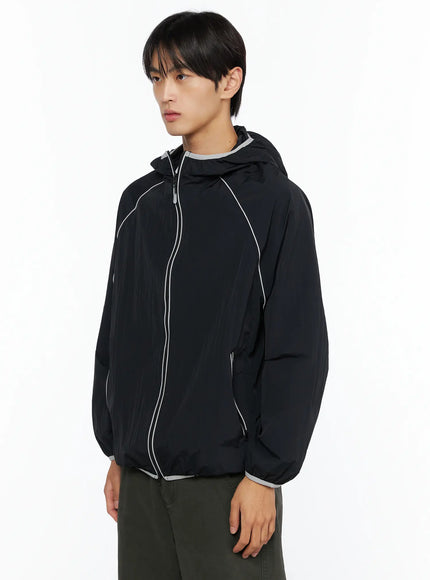 Men's Two-Tone Windbreaker IL528 Black angled front side view on male model, showing curved reflective piping across chest and side zip pocket