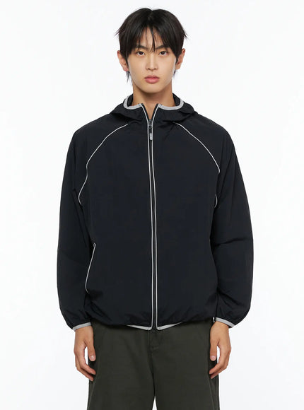 Men's Two-Tone Windbreaker IL528 Black front cropped view on male model, hands relaxed, hooded nylon jacket with grey contrast hood lining