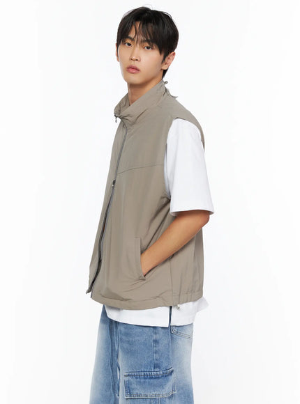 Men's Two-Way Anorak Vest IL515 light beige side shot on male model with hand in pocket, showing stand collar, front zip, and lightweight nylon texture