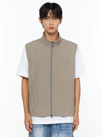 Men's Two-Way Anorak Vest IL515 light beige front shot on male model showing full zipper, stand collar, and relaxed fit over white tee