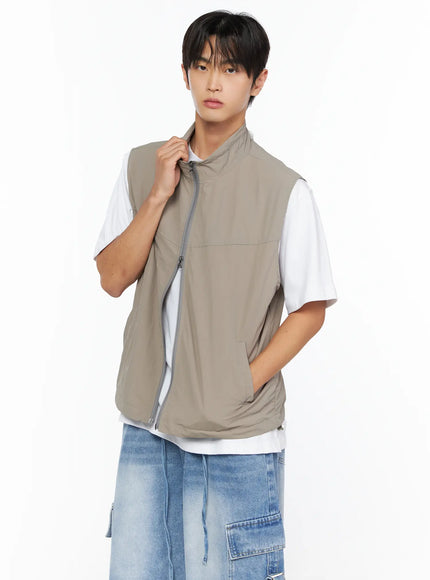 Men's Two-Way Anorak Vest IL515 light beige close-up front on male model pulling collar, layered over white tee with denim shorts