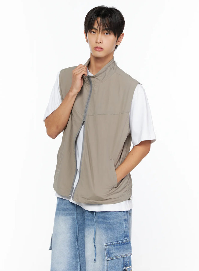 Men's Two-Way Anorak Vest IL515 light beige close-up front on male model pulling collar, layered over white tee with denim shorts