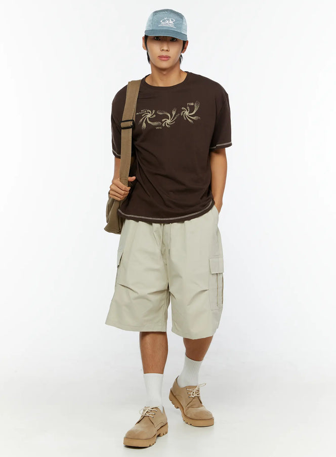 LEWKIN Men's Utility Cargo Shorts IL513 Beige full-length front view on male model styled with brown graphic tee, crossbody bag, cap and suede shoes