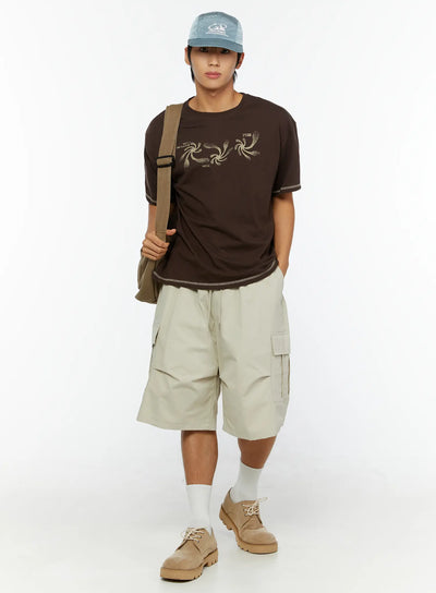 LEWKIN Men's Utility Cargo Shorts IL513 Beige full-length front view on male model styled with brown graphic tee, crossbody bag, cap and suede shoes