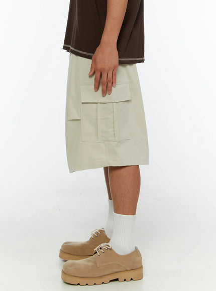 Men's Utility Cargo Shorts IL513 Beige side view on model with hand resting on cargo pocket, showing relaxed wide-leg cut and length