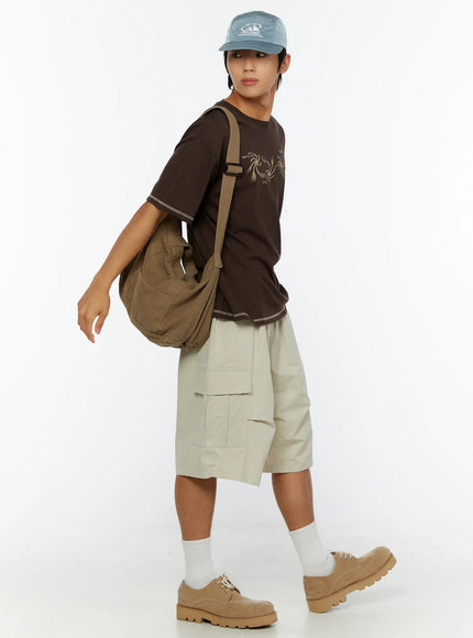 Men's Utility Cargo Shorts IL513 Beige full-length side view on model walking with shoulder bag and cap, showcasing relaxed cargo silhouette