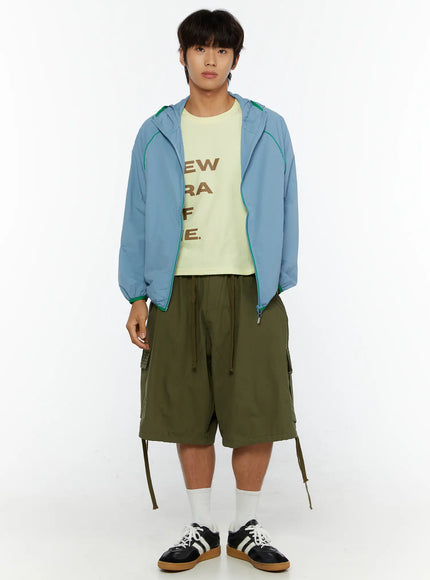 Men's Utility Pocket Cargo Shorts IL515 olive green full front view on male model standing styled with blue windbreaker and graphic tee