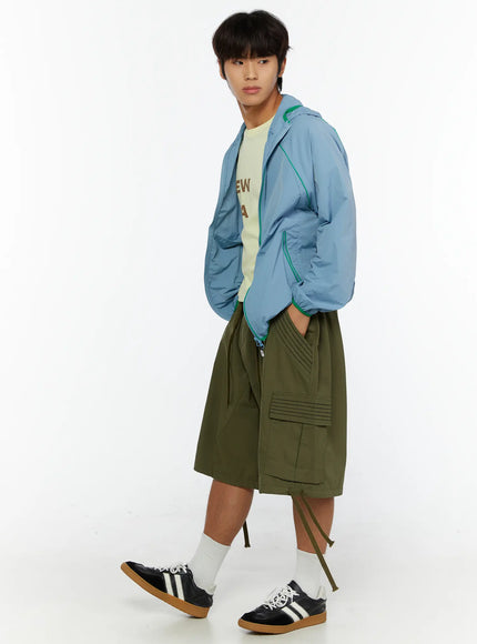 Men's Utility Pocket Cargo Shorts IL515 olive green three-quarter side view on male model walking styled with blue hooded jacket and sneakers