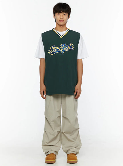 Men's Varsity Style Graphic Tank IL509 green front shot on male model standing straight with New York script graphic and striped V-neckline over white tee