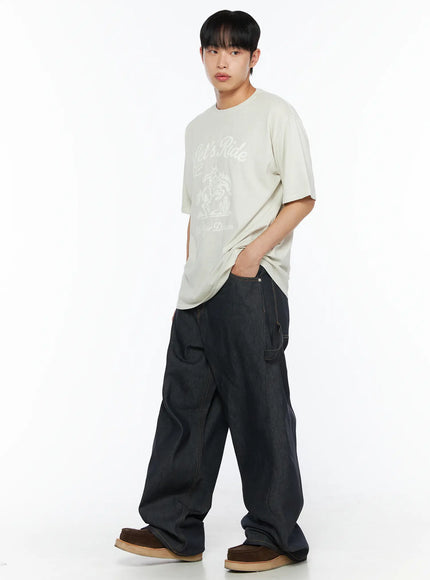 Men's Washed Wide Leg Jeans IL510 Black three-quarter front shot on male model in cream Let's Ride tee with hand in pocket showing wide-leg denim and brown loafers