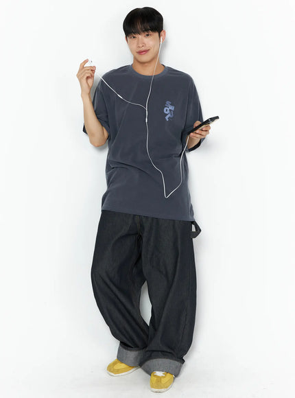 Men's Washed Wide Leg Jeans IL510 Black full-length front shot on male model in charcoal SEOUL graphic tee with earphones and MP3 player, yellow sneakers and rolled hem