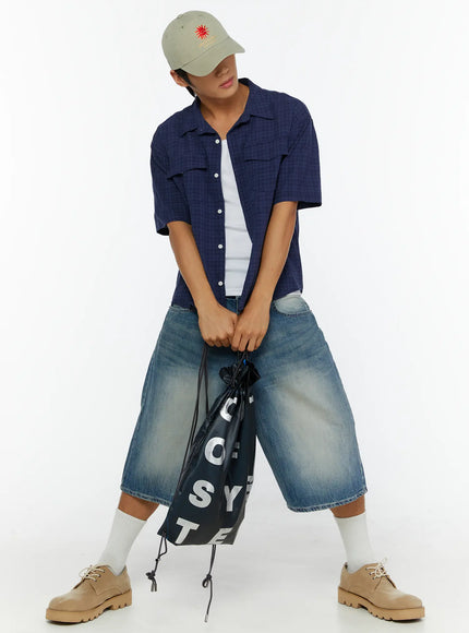 Men's Washed Wide Leg Jorts IL513 Blue front full-body shot on model holding drawstring bag downward, wide leg washed denim with cap and navy check shirt styling