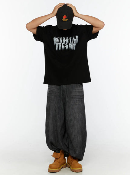 Men's Wide Leg Balloon Jeans IL515 Black front full-body on male model standing with face hidden under black cap, styled with black graphic tee and tan boots